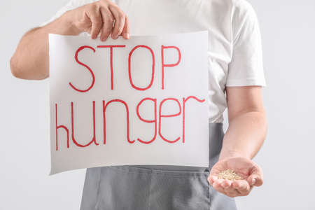 Man holding paper sheet with text STOP HUNGER and wheat grains on light backgroundの写真素材