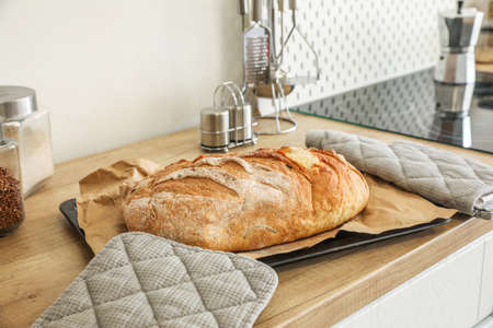 Baking sheet with fresh bread and oven mittens on counter in kitchen