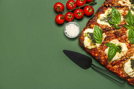 Tasty Italian pie with mozzarella, pesto sauce, salt and tomatoes on green background