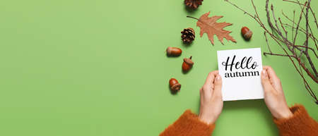 Woman holding card with text HELLO AUTUMN and floral decor on green background with space for textの写真素材