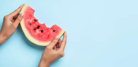 Hands with slice of fresh watermelon on blue background with space for textの写真素材