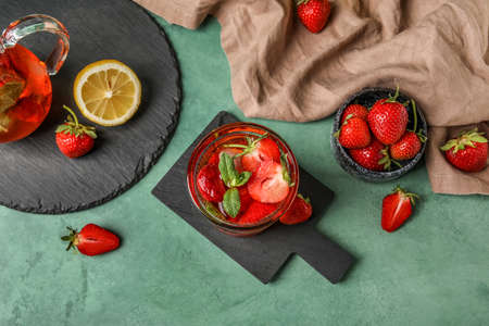 Board with glass of strawberry lemonade on green background