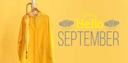 Text HELLO SEPTEMBER and rack with raincoat and umbrella on yellow backgroundの写真素材