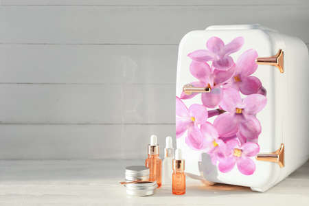 Small refrigerator with floral print and cosmetic products on light wooden backgroundの写真素材