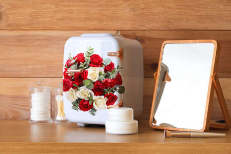 Small cosmetic refrigerator with floral print, supplies and mirror on wooden backgroundの写真素材