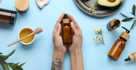 Female hands with bottle of essential oil, cosmetics and natural ingredients on blue backgroundの写真素材