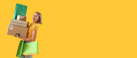 Pretty young woman with credit card, parcels and shopping bags on yellow background with space for text. online shoppingの写真素材