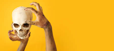 Hands of zombie with human skull on yellow background. halloween concept