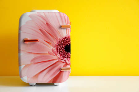 Small cosmetic refrigerator with floral print on table near yellow wallの写真素材