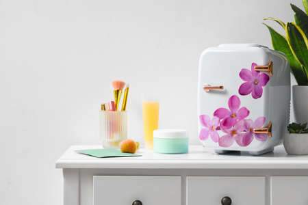 Small refrigerator with floral print and cosmetic products on table in roomの写真素材