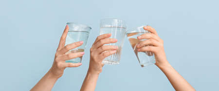 Female hands with glasses of water on light blue background