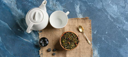 Composition with dry tea leaves, cup, teapot and blueberry on color backgroundの写真素材