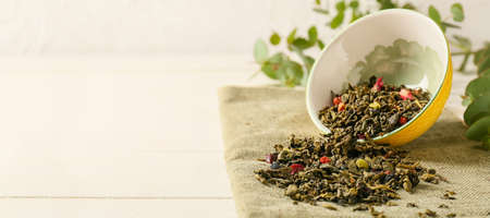 Bowl with dry green tea leaves on light background with space for text