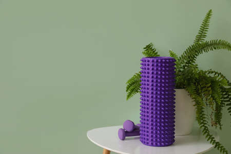 Table with foam roller, dumbbells and houseplant near green wallの写真素材