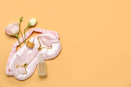 Facial massage tool with cosmetic dropper bottle, sleeping mask and roses on beige backgroundの写真素材