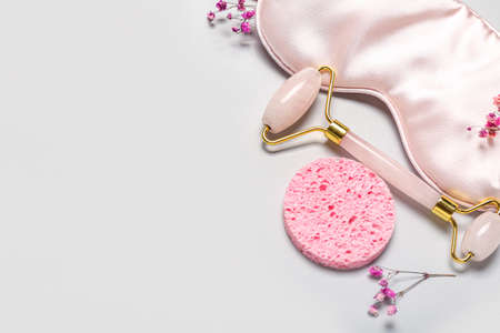 Facial massage tool with sponge, sleeping mask and flowers on light backgroundの写真素材
