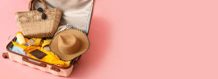 Open suitcase with clothes and beach accessories on pink background with space for textの写真素材