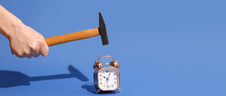 Hand with hammer and alarm clock on blue backgroundの写真素材