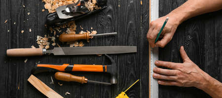 Carpenter applying marking onto plank on dark wooden background, top viewの写真素材