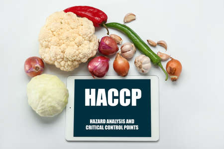 Tablet computer with text HAZARD ANALYSIS AND CRITICAL POINTS and fresh vegetables on light backgroundの写真素材