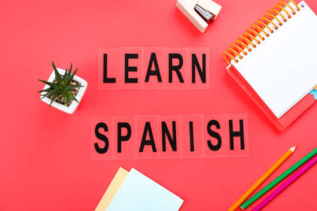 Text LEARN SPANISH with stationery and flowerpot on red background