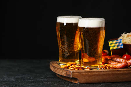 Board with glasses of beer, food and flags on table against dark background. Oktoberfest celebrationの写真素材