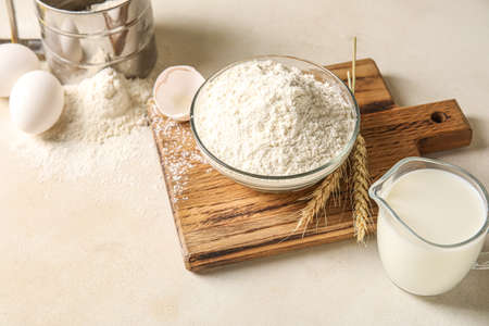 Bowl with flour, eggs, jug with milk and wheat ears on white tableの写真素材