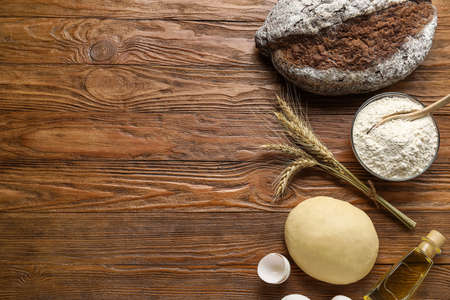Fresh rye bread, bowl of flour, spikelets, raw dough, oil and eggs on wooden backgroundの写真素材