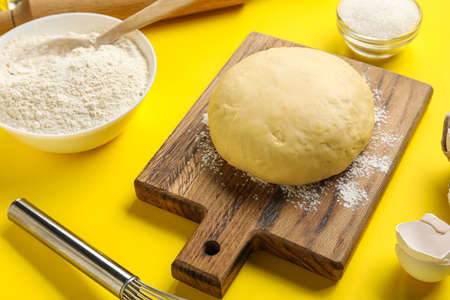 Wooden board with raw dough on yellow backgroundの写真素材