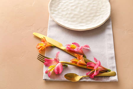 Table setting with plate, cutlery and alstroemeria flowers on beige backgroundの写真素材