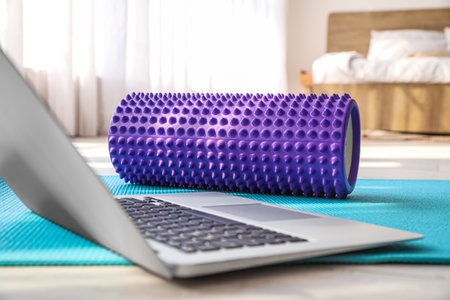 Foam roller and laptop on fitness mat in room, closeupの写真素材
