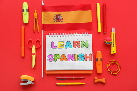 Notebook with text LEARN SPANISH, flag and stationery supplies on red background