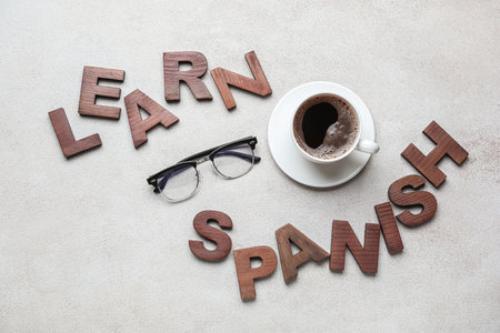 Text LEARN SPANISH with eyeglasses and cup of coffee on gray background