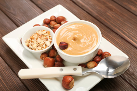 Plate with bowls of tasty nut butter and hazelnuts on wooden background, closeupの写真素材