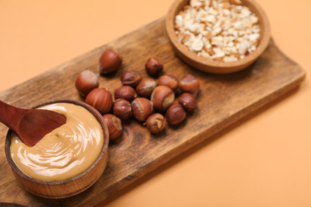 Wooden board with bowl of tasty nut butter and hazelnuts on color background, closeupの写真素材