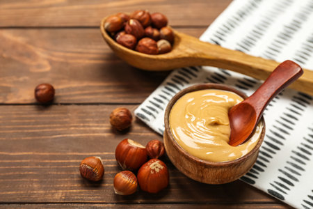 Bowl of tasty nut butter and spoon with hazelnuts on wooden backgroundの写真素材