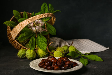 Plate with fresh chestnuts on dark background