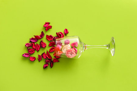 Overturned wine glass with flowers and rose petals on green backgroundの写真素材