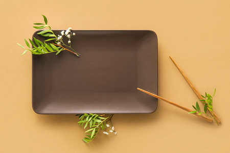 Plate, chopsticks and floral decor on beige background