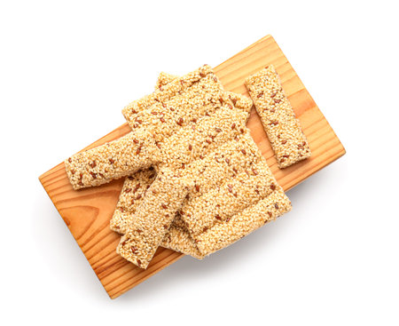 Wooden board with tasty sesame kozinaki on white backgroundの写真素材