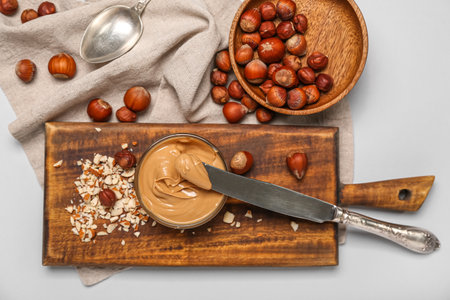 Wooden board with bowl of tasty nut butter and hazelnuts on white backgroundの写真素材