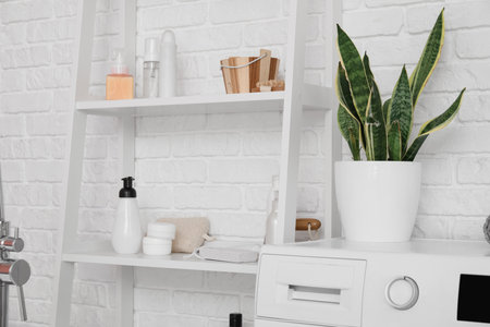Shelf unit with bath accessories and houseplant on washing machine near white brick wallの写真素材