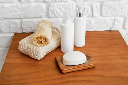 Bath accessories on wooden table near white brick wall