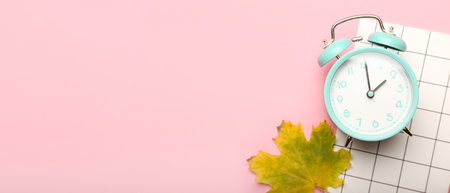 Alarm clock, notebook and autumn leaf on pink background with space for textの写真素材