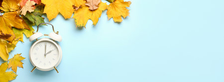 Alarm clock and autumn leaves on light blue background with space for text