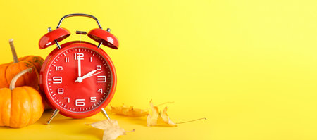 Alarm clock and autumn leaves with pumpkins on yellow background with space for textの写真素材