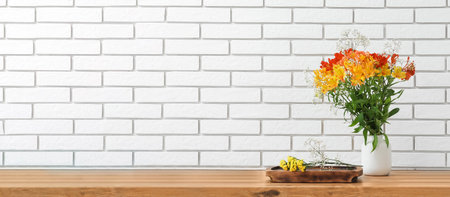 Vase with bouquet of beautiful alstroemeria flowers on table against white brick background with space for textの写真素材