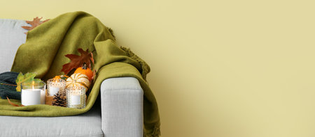 Burning candles with plaid and autumn decor on sofa near color wall with space for textの写真素材
