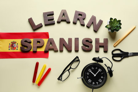 Text LEARN SPANISH, stationery, flag, alarm clock and eyeglasses on beige backgroundの写真素材