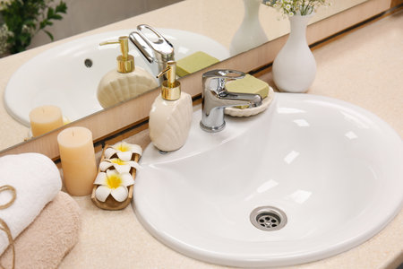 Bath accessories with sink, flowers and candle on table in bathroomの写真素材